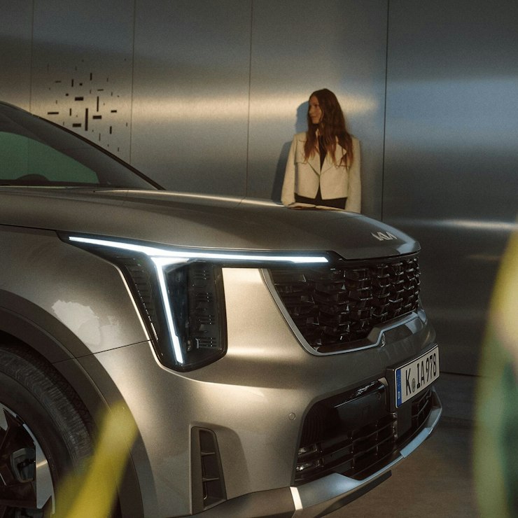 Eine Frau steht neben der Frontpartie des neuen Kia Sorento