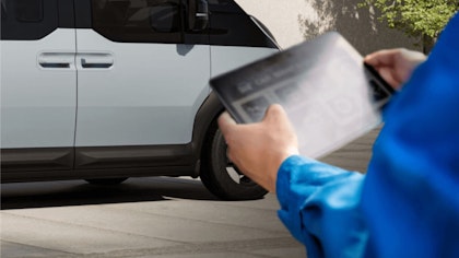 Nahaufnahme von Händen, die ein digitales Gerät in der Nähe eines Fahrzeugmotors nutzen, zur Illustration des Echtzeitzugangs zu den Kia FMS (Flottenmanagementlösungen) und Datendiensten
