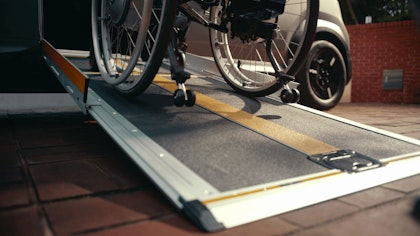 Eine Person im Rollstuhl fährt vom Trottoir über die seitliche Rampe in einen Kia WAV.