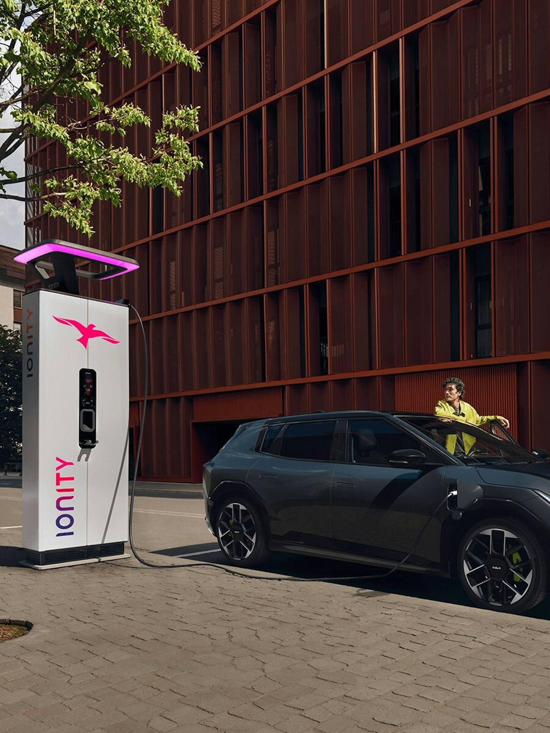 Ein Mann steht beim Kia EV4 GT, welcher an einer öffentlichen Station auflädt