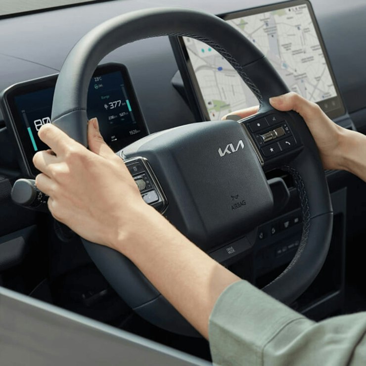 Fahrer am Lenkrad des Kia&nbsp;PV5&nbsp;WAV mit Hands-On-Erkennung, die den Handkontakt überwacht und so zu einer sicheren Fahrt beiträgt.