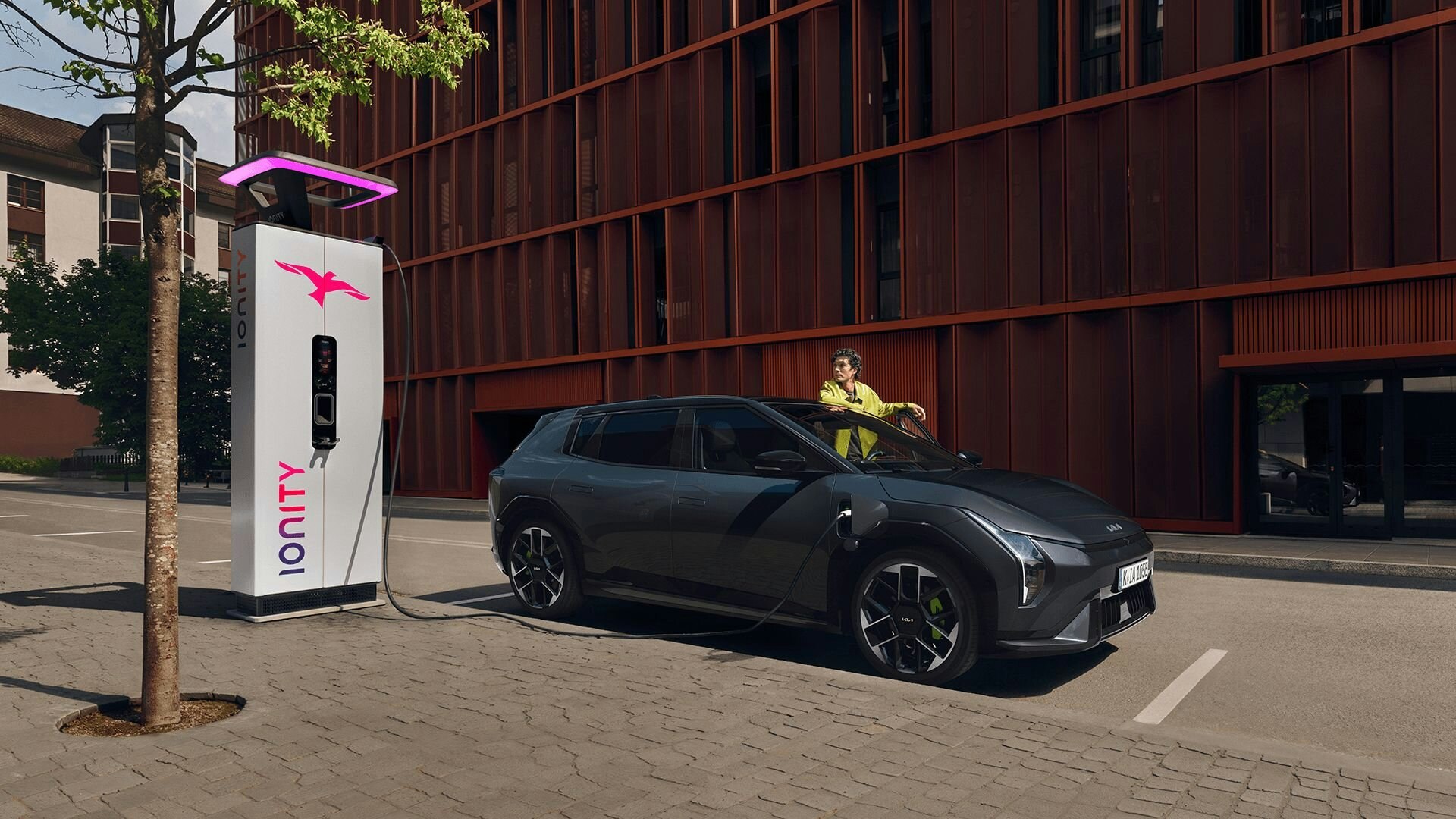 Ein Mann steht beim Kia EV4 GT, welcher an einer öffentlichen Station auflädt